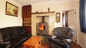 A living room with a wood-burning stove, a dark patterned sofa, a wooden coffee table, and a patterned armchair. - Sleep 6 Cottage -petsok, Selfcheck-in, Freeparking (Ardara)