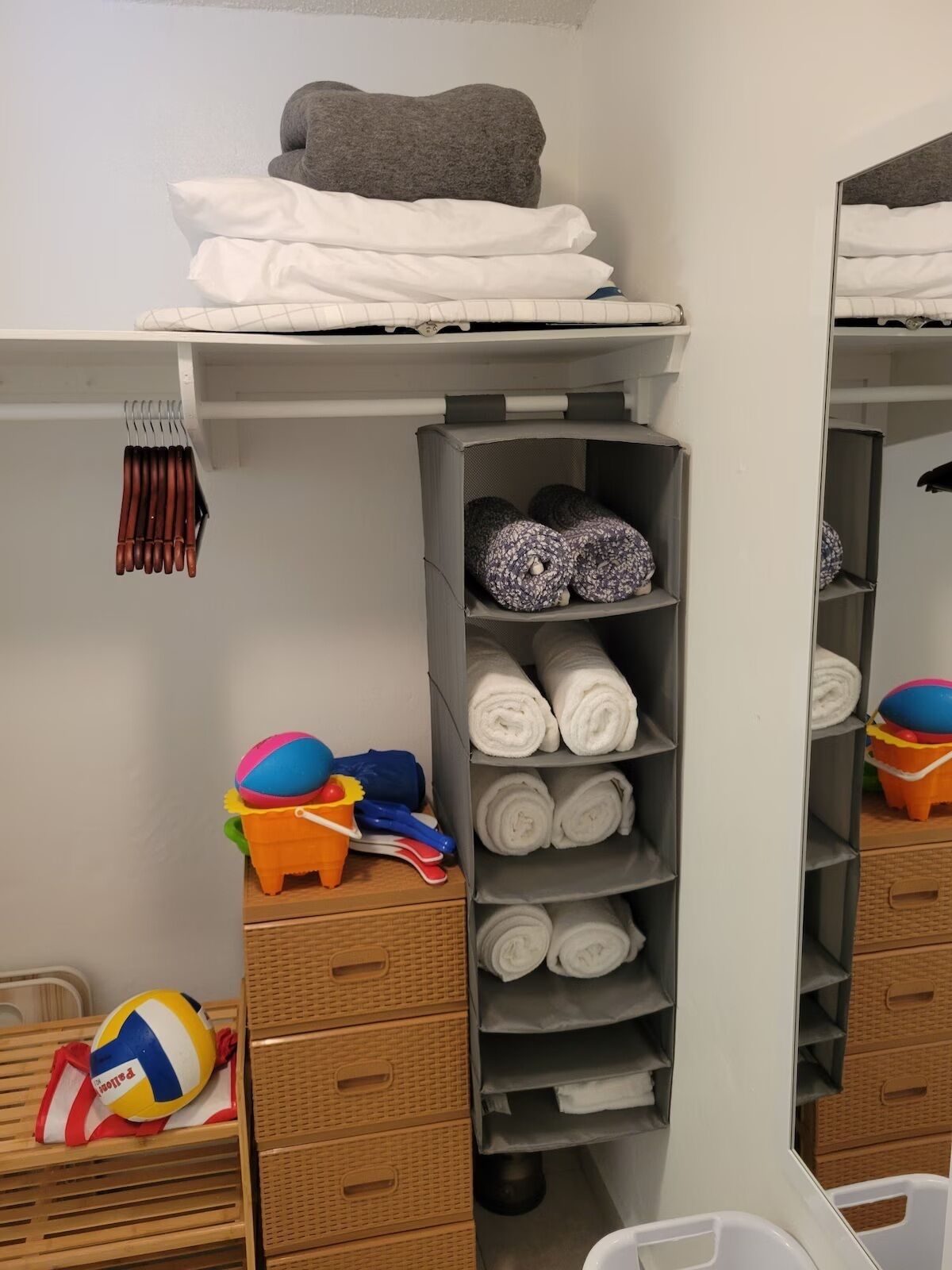 A storage area with shelves holding towels and rolled-up items, a shelf with folded clothes, and a small table with beach toys.