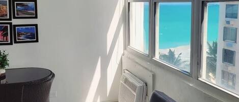 A room with a view of the sea, a dining table, a sofa, and several framed pictures on the wall.