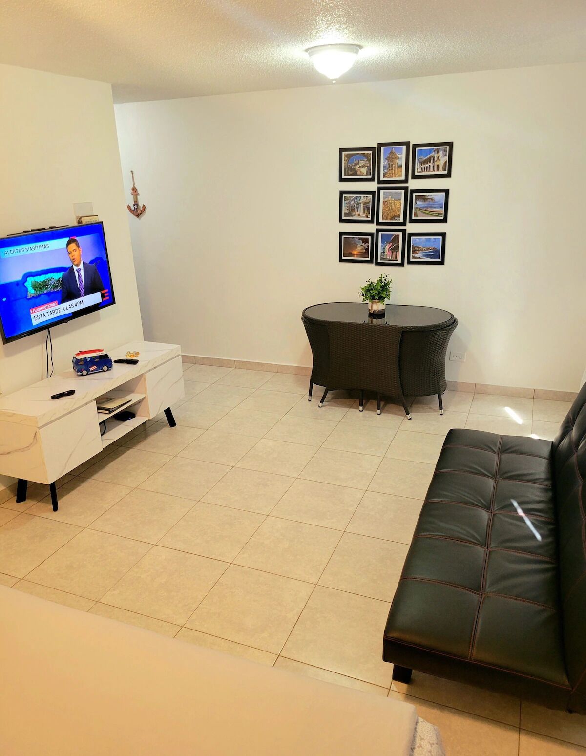 Ein Wohnzimmer mit Fernseher, einer Couch, einem runden Tisch mit Stühlen und einer Wand mit gerahmten Bildern.