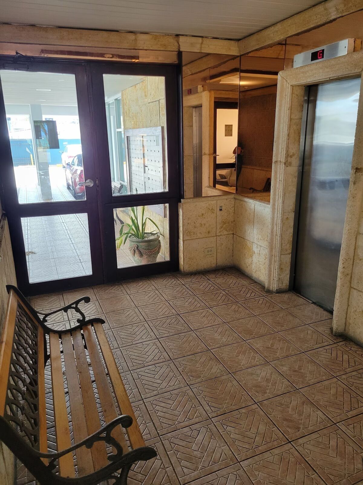 A corner area with a bench, a potted plant, a tiled floor, and an elevator.
