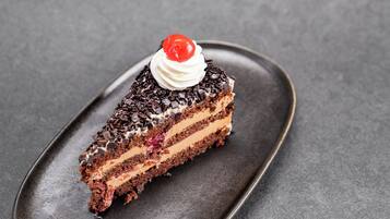 Una rebanada de pastel de chocolate en capas con crema batida y una cereza encima, sobre un plato oscuro.