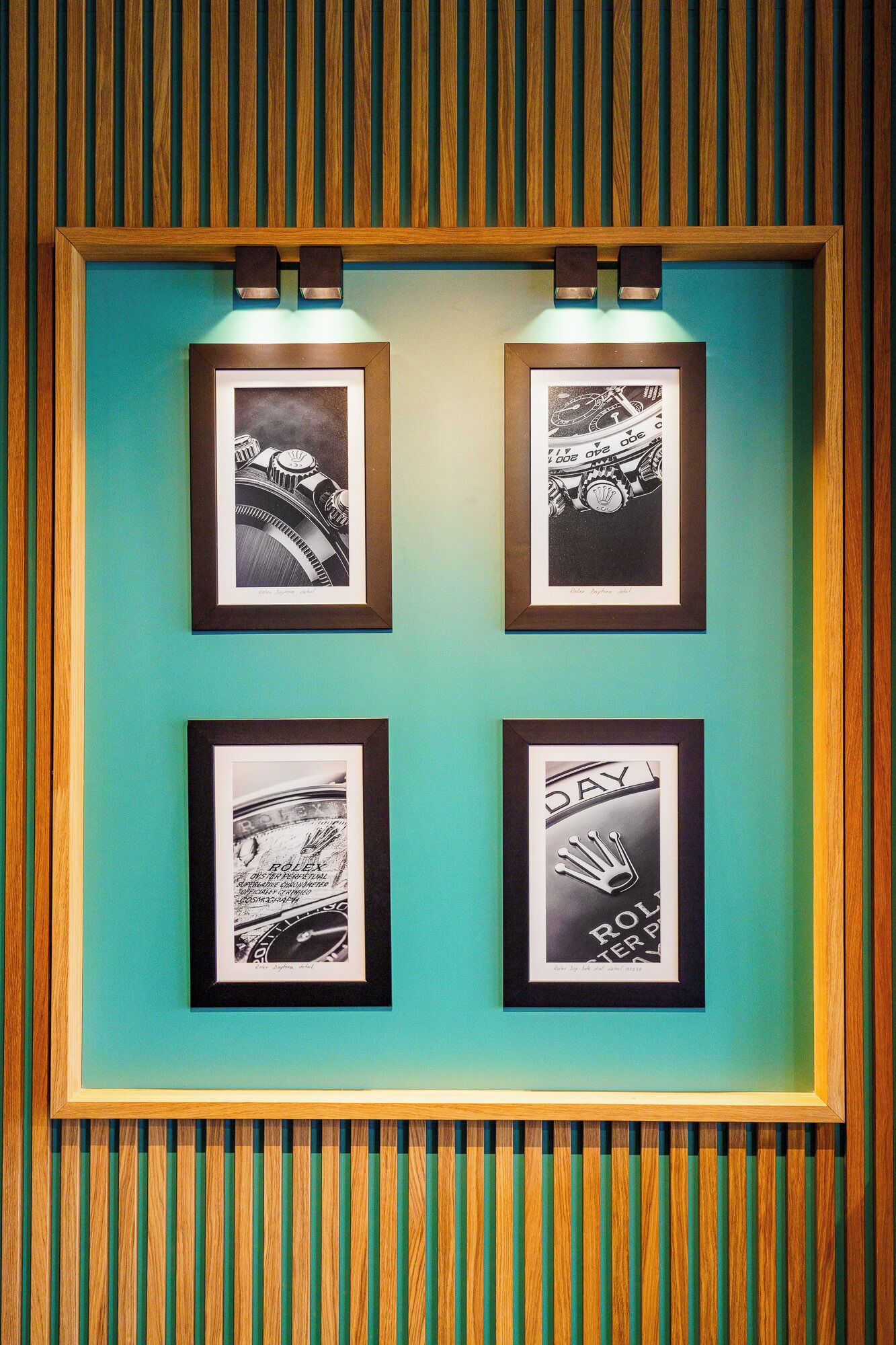 A framed artwork display with four pieces, each depicting different mechanical or industrial themes, set against a teal wall with a wooden panel border.
