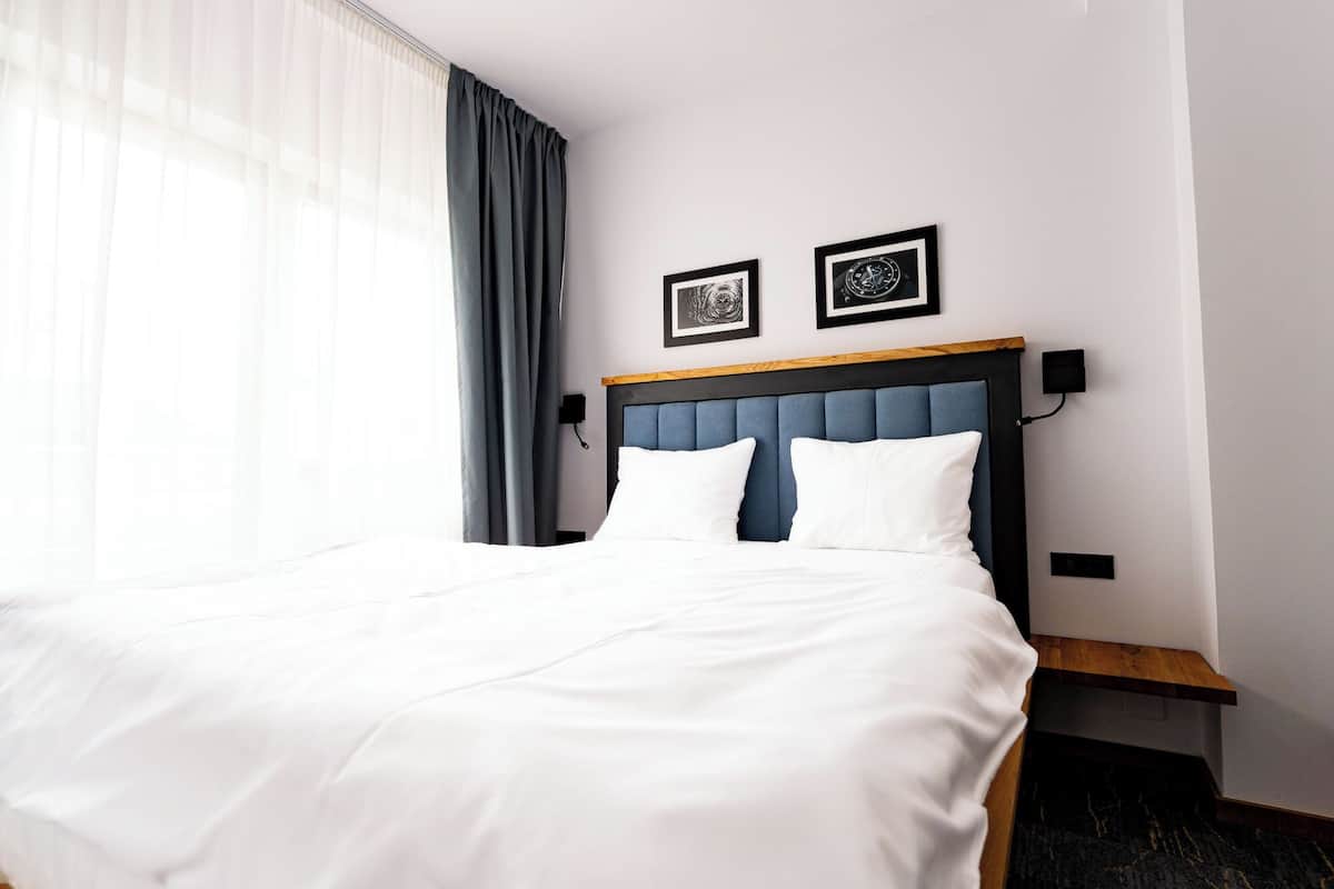 A neatly made bed with white linens, a blue upholstered headboard, and two framed pictures on the wall.