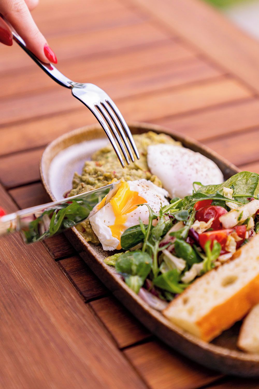 Un plato de desayuno con huevos pochados, vegetales de hoja verde y pan sobre una mesa de madera.