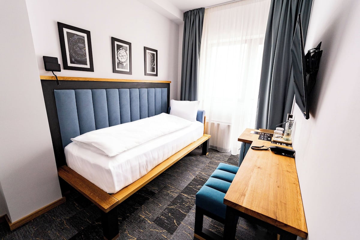 A hotel room with a bed, a desk, a chair, and a TV mounted on the wall.
