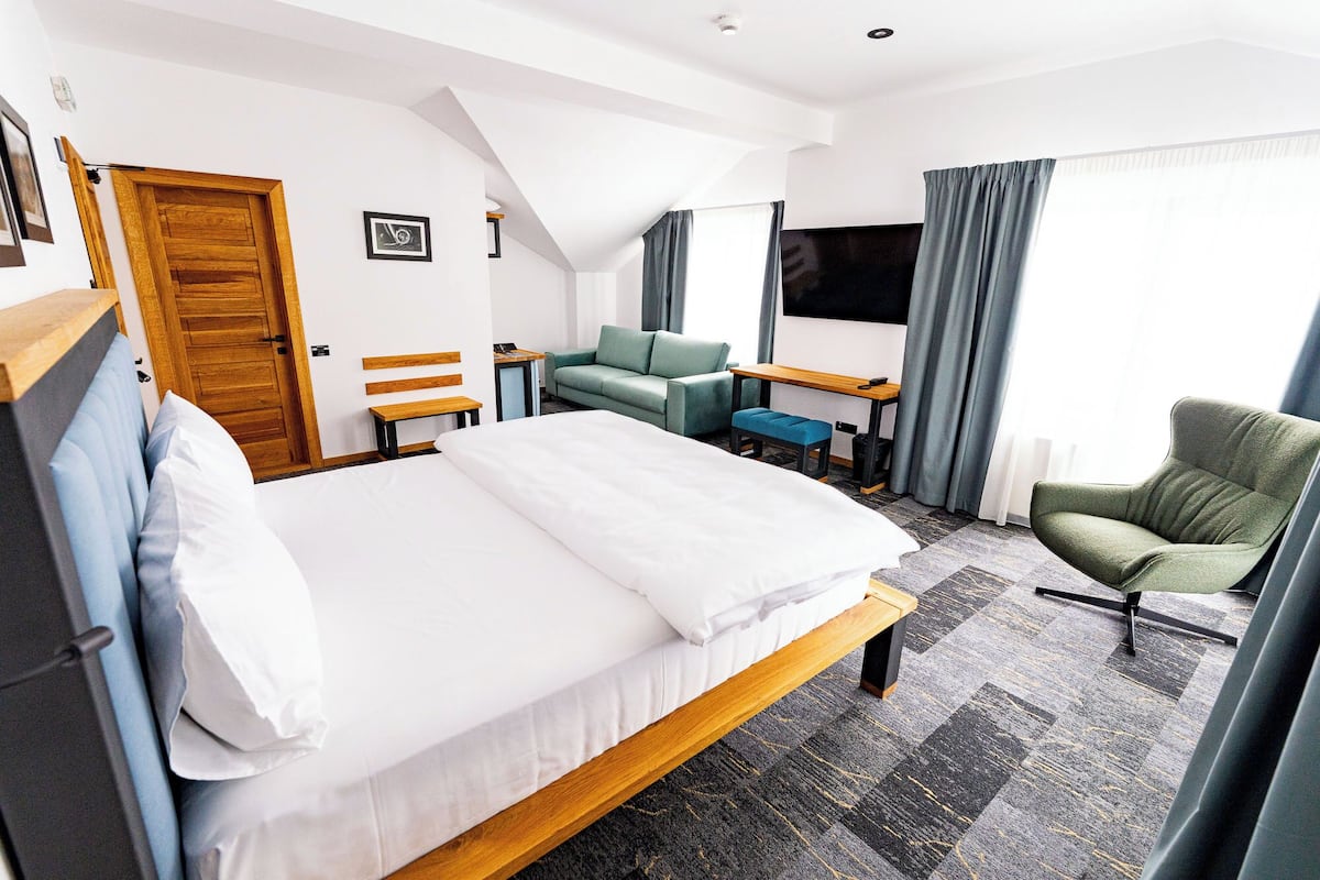 A hotel room with a bed, a desk, a chair, a sofa, and a TV.