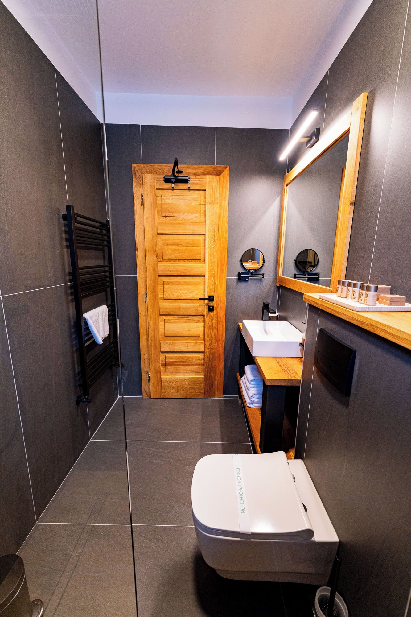 A modern bathroom with a wooden door, a white sink, a towel rack, and a mirror.