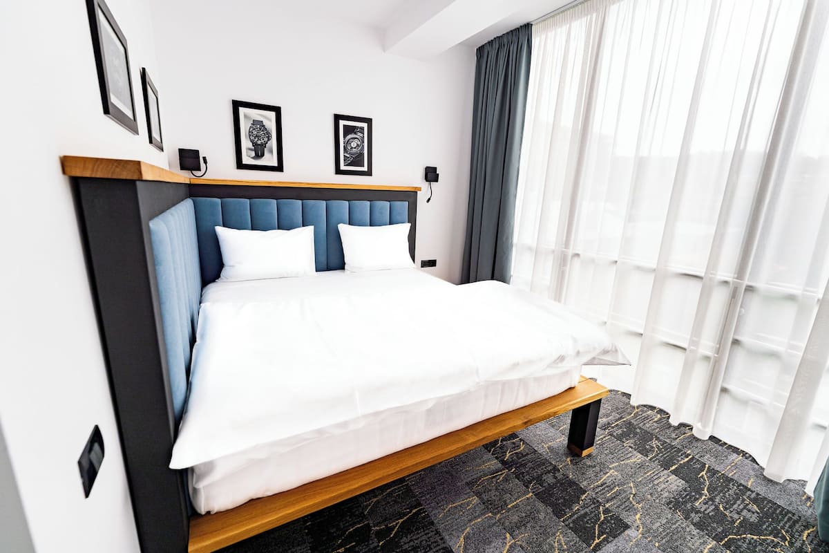 A neatly made bed with white linens, a blue upholstered headboard, and a black and grey patterned carpet.