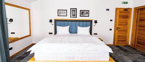 A hotel room with a bed, a wooden headboard, a blue accent, framed pictures on the wall, and a wooden door.