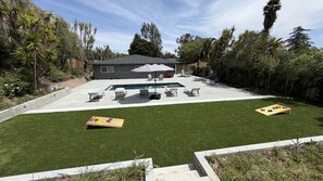 Un patio trasero con piscina, mobiliario exterior y un césped bien cuidado.