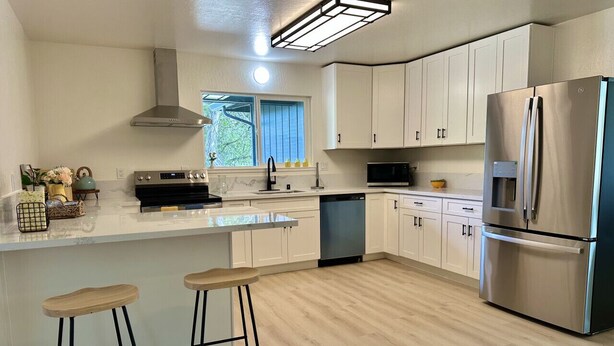 A modern kitchen with white cabinets, a stainless steel refrigerator, a dishwasher, and wooden bar stools. - Beautiful 4 BD home, 1.5 Miles from the Beach (Soquel)