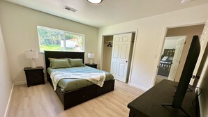A bedroom with a bed, bedside tables, a TV stand, and a window with a view of greenery. - Beautiful 4 BD home, 1.5 Miles from the Beach (Soquel)