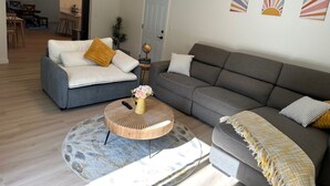 A living room with a grey sofa, a white sofa, and a round coffee table with a vase. There are three wall art pieces above the grey sofa. - Beautiful 4 BD home, 1.5 Miles from the Beach (Soquel)