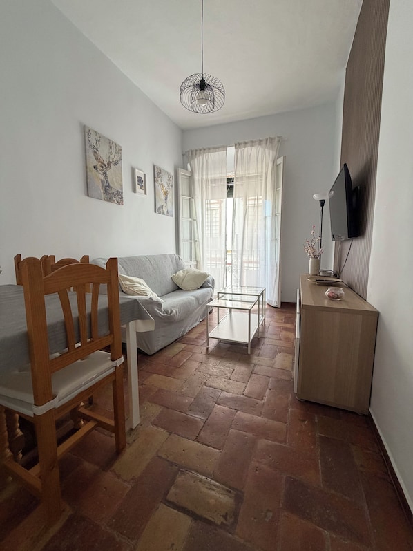 Una habitación con cama, una silla de madera, una mesita, televisor y obras de arte en las paredes.