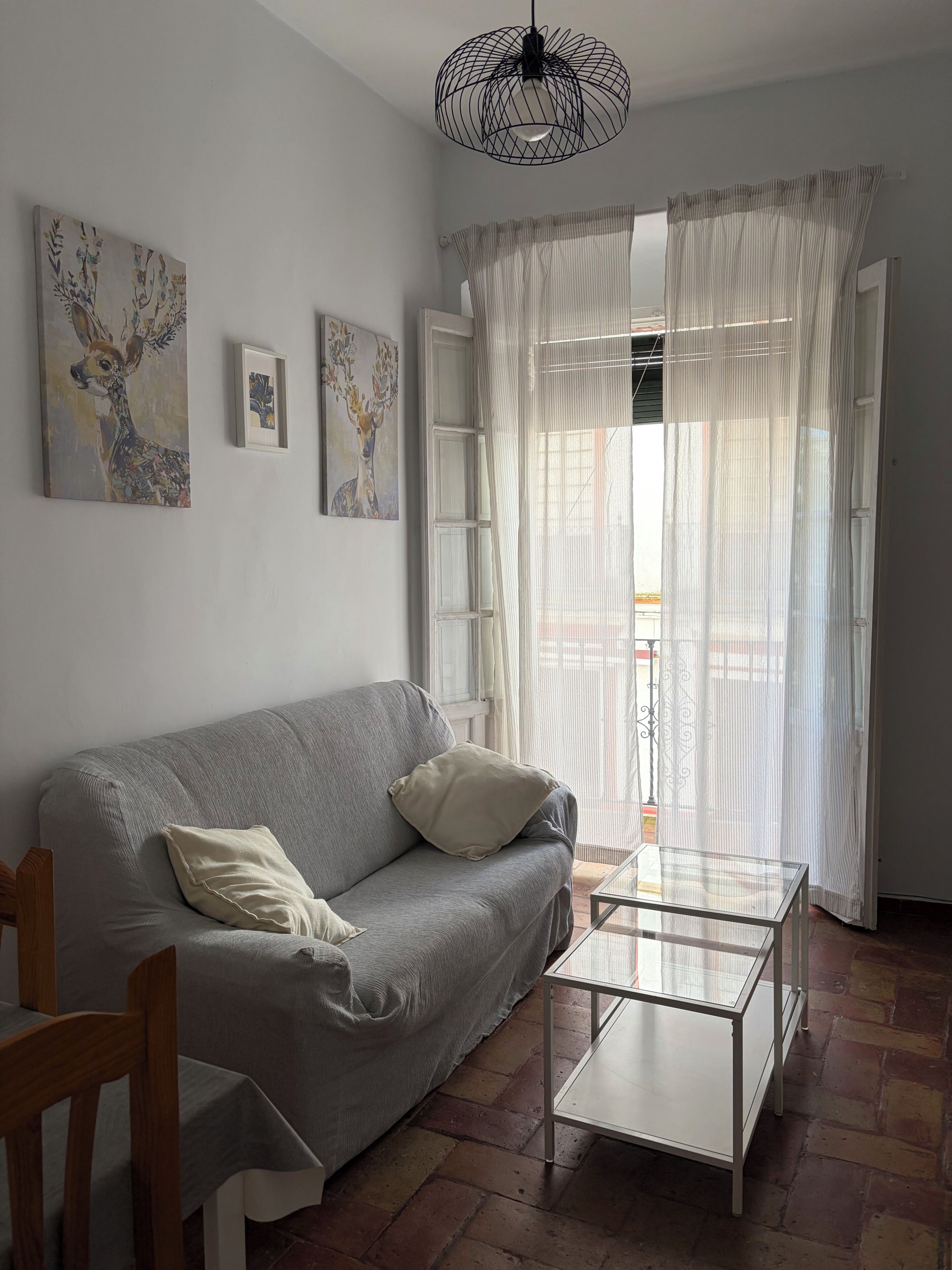 A living room with a grey sofa, a glass coffee table, and artwork on the wall.
