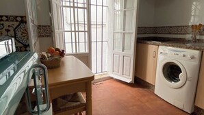 Una cuina petita amb rentadora, taula de menjador i caires, i una finestra amb reixetes.