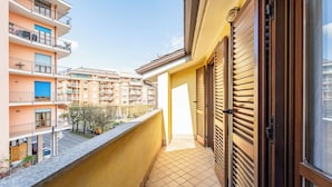 A narrow balcony with a tiled floor, a wooden door, and a view of adjacent buildings.