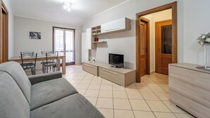 A modern living room with a sofa, TV, and a dining area with chairs and a table.