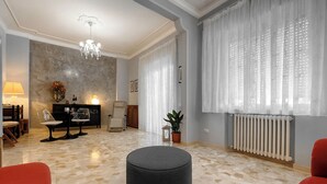 A spacious living room with a round ottoman, a chandelier, and a large window with sheer curtains. - Luminous Viola room with artistic light - Madame Fanny (Lucca)