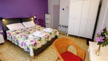 A bedroom with a bed, a wicker chair, a wardrobe, and a small table with a vase.