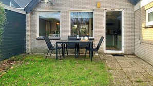 A brick house with a patio table and chairs, a satellite dish, and a sliding glass door. - Bungalow in Sint Maartenszee Near Beach (Sint Maartensvlotbrug)