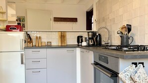 A modern kitchen with a built-in oven, a stove, and a sink. There is a wooden cutting board and various kitchen utensils on the countertop. - Bungalow in Sint Maartenszee Near Beach (Sint Maartensvlotbrug)