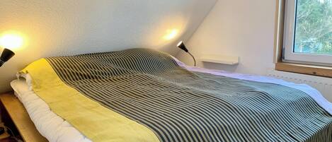 Un dormitorio con cama, mesita de noche, lámpara, ventana y radiador.