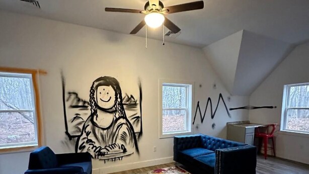 Una habitación con ventilador de techo, un mural grande en la pared, un sofá azul, una alfombra colorida y un escritorio con una silla.