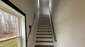 Una escalera estrecha con un rellano alfombrado y una ventana con vista a un área verde.