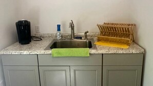 Una pequeña cocina con encimera de granito, un lavamanos, una cafetera, una botella de jabón para manos y un tendedero.
