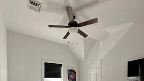 Un dormitorio con una cama, ventilador de techo, ventana con persianas, puerta y cómoda.