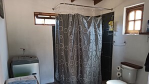 A bathroom with a toilet, a shower curtain, a towel rack, and a small window.