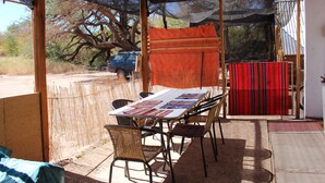 An outdoor dining area with a table and chairs, a covered seating area, and a view of a tree and a parked car.