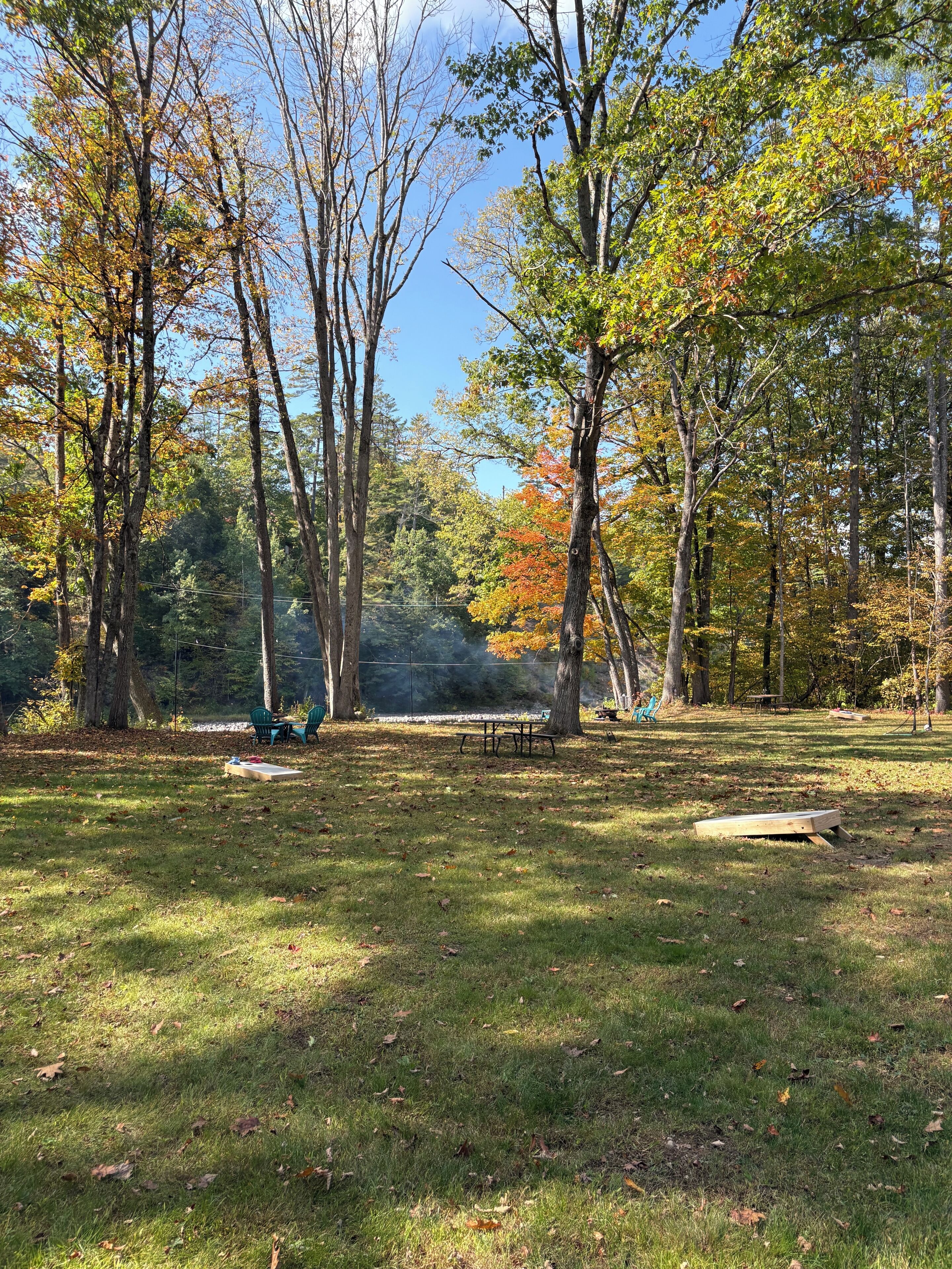 A park with picnic tables and chairs, surrounded by trees with autumn foliage.