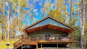 A cabin with a wooden deck, a covered porch, and a stone foundation.