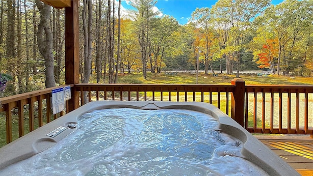 A hot tub on a wooden deck with a view of a forest and a lake.