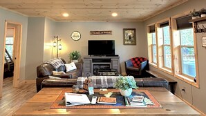 A spacious living room with a large wooden coffee table, leather sofas, a flat-screen TV, and a fireplace.