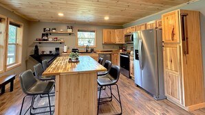 A modern kitchen with wooden cabinets, a central island with chairs, stainless steel appliances, and a window providing natural light.