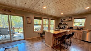 A spacious kitchen with wooden cabinets, a central island with bar stools, large windows, and a view of the outdoors.