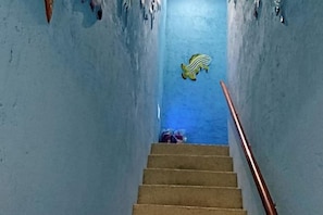 Una scala con corrimano che conduce a una stanza con un muro blu e un oggetto a righe gialle e bianche.