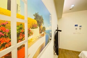 A corridor with a mural of a coastal scene, a coat rack, and a bed with a white cover. - Kenting Nanwan 254 (Pingtung)