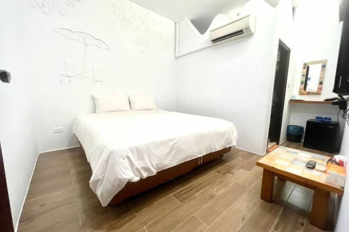 Una camera da letto con un letto, un pavimento in legno, un tavolino e un condizionatore d'aria a parete.