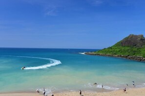 Une plage à l’eau turquoise et limpide, un promontoire rocheux, et des gens qui profitent du bord de mer.