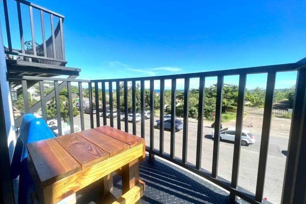 Un balcone con una panca di legno, una ringhiera metallica e vista su un parcheggio e del verde.