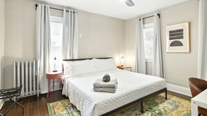 Ein ordentlich eingerichtetes Schlafzimmer mit einem Bett, einem Heizkörper, einer Stehlampe und einem gerahmten Bild an der Wand.