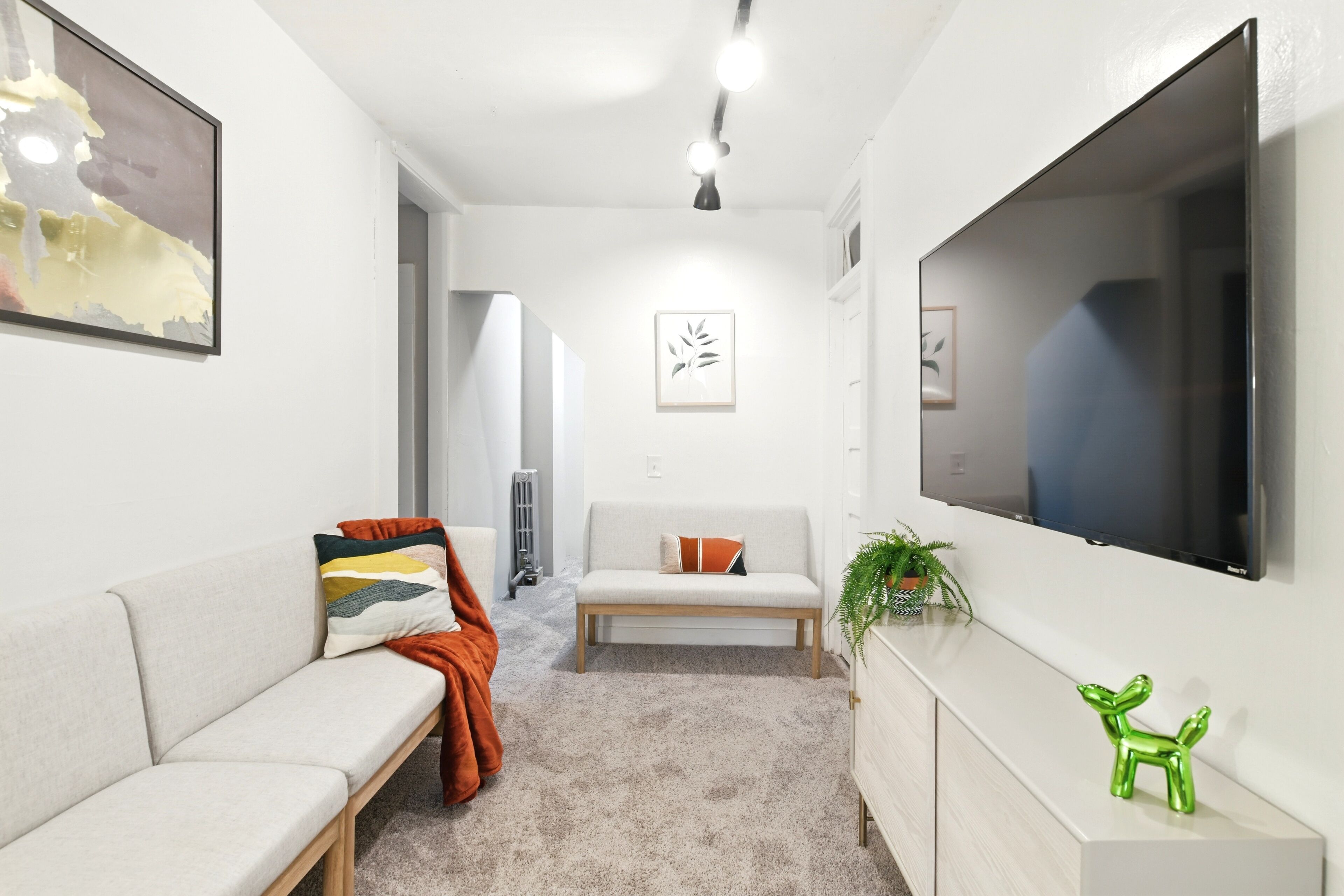 Un salon moderne avec un canapé, un banc, un téléviseur et un petit objet décoratif vert.