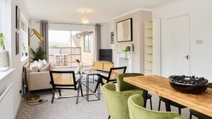 En spiseplads med et træbord og grønne stole, en gulvlampe og udsigt til en balkon med udendørs møbler.