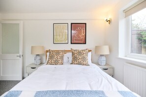 A neatly arranged bedroom with a large bed, two bedside tables with lamps, and two framed artworks on the wall.