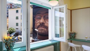 Ett rum med ett stort fönster, ett element, ett glasbord och vita stolar.